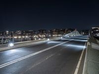 a car is driving down the street at night, by a bridge with traffic lights on