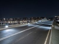 a car is driving down the street at night, by a bridge with traffic lights on