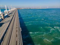 a bridge over the ocean with construction equipment in the background and two people walking on it