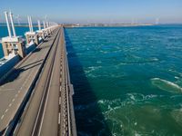 a bridge over the ocean with construction equipment in the background and two people walking on it