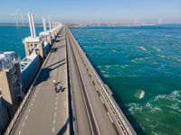 a bridge over the ocean with construction equipment in the background and two people walking on it