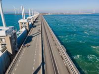 a bridge over the ocean with construction equipment in the background and two people walking on it