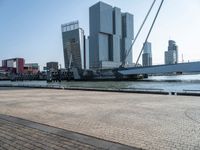 a brick walkway next to the water in front of buildings with cranes on them and some red boats