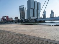 a brick walkway next to the water in front of buildings with cranes on them and some red boats