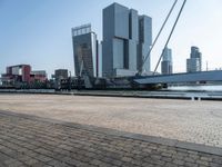 a brick walkway next to the water in front of buildings with cranes on them and some red boats