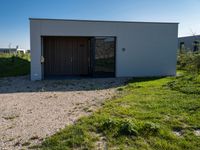 the large building has a door open near a driveway with grass on the side of it