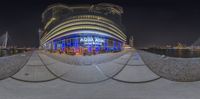 a fish eye view at night with blue lights in the background, including a boat dock and buildings