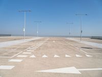 white arrows are shown on the parking lot of an airport in the day time, with three light poles and three light pole poles