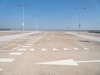 white arrows are shown on the parking lot of an airport in the day time, with three light poles and three light pole poles