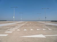 white arrows are shown on the parking lot of an airport in the day time, with three light poles and three light pole poles