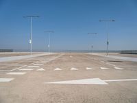 white arrows are shown on the parking lot of an airport in the day time, with three light poles and three light pole poles