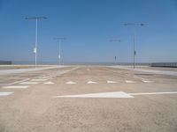 white arrows are shown on the parking lot of an airport in the day time, with three light poles and three light pole poles