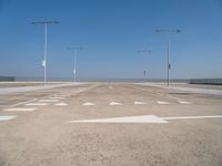 white arrows are shown on the parking lot of an airport in the day time, with three light poles and three light pole poles