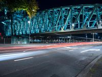 a steel bridge above the city at night, seen from under the street lights of cars on the side