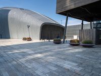 a brick patio with planters and a large metal building in the background, also two smaller cement planters