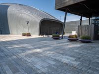 a brick patio with planters and a large metal building in the background, also two smaller cement planters