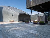 a brick patio with planters and a large metal building in the background, also two smaller cement planters