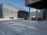 a brick patio with planters and a large metal building in the background, also two smaller cement planters