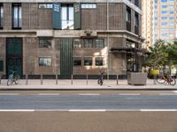 an image of people riding bikes and two parked bikes on street in urban area with building in background