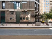 an image of people riding bikes and two parked bikes on street in urban area with building in background