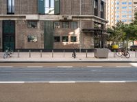 an image of people riding bikes and two parked bikes on street in urban area with building in background