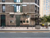 an image of people riding bikes and two parked bikes on street in urban area with building in background