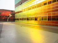 a yellow and green building with many windows reflecting it's sunlight from the window of a nearby building