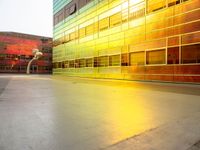 a yellow and green building with many windows reflecting it's sunlight from the window of a nearby building