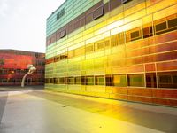 a yellow and green building with many windows reflecting it's sunlight from the window of a nearby building