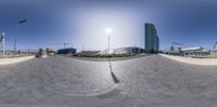 this is a fisheye image of an empty space with buildings in the background and a person skateboarding