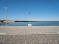 a parking lot near the sea in front of a large wind turbine plant and a body of water