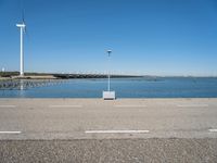 a parking lot near the sea in front of a large wind turbine plant and a body of water