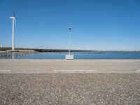 a parking lot near the sea in front of a large wind turbine plant and a body of water