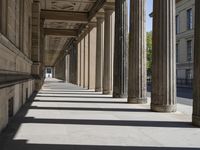 an empty sidewalk with pillars and some buildings in the background, casting shadows on it