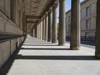 an empty sidewalk with pillars and some buildings in the background, casting shadows on it