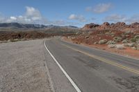 an empty road is winding through some desert land and mountains in the distance with a lone motorcycle on the side