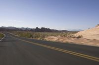 a person rides down an empty road in the mountains of the desert with mountains behind him