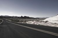 a person rides down an empty road in the mountains of the desert with mountains behind him