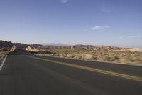 a person rides down an empty road in the mountains of the desert with mountains behind him