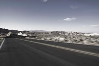 a person rides down an empty road in the mountains of the desert with mountains behind him