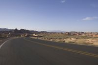 a person rides down an empty road in the mountains of the desert with mountains behind him