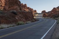 a long road lined with red rocks in the desert near a rock formation and desert area