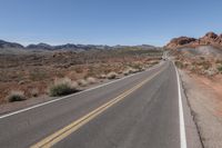 the desert landscape features a deserted paved highway and some mountains in the background there are bushes on either side of the road