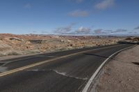 a lone motorist rides down the road next to some rocks and desert with mountains