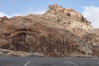 a car is parked in the parking lot by some mountainside structures with rocks and a few bushes on the road