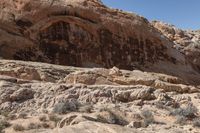 a man riding a motorcycle past a rock formation in the desert and hills with blue sky