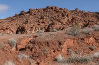 people riding on horseback through the desert on a trail in the distance are red mountains