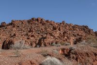 people riding on horseback through the desert on a trail in the distance are red mountains