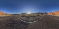 a wide angle view of a desert road, with a mountain in the background and a red rock formation