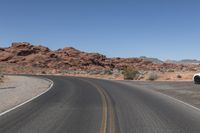 two motorcycles driving on the middle of a desert road in the daytime, there is no one visible